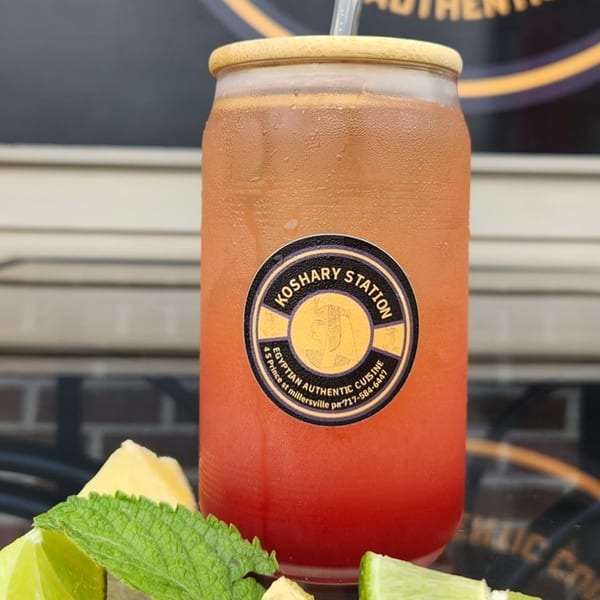 A refreshing red and orange drink in a glass with a Koshary Station label, garnished with mint and lime.