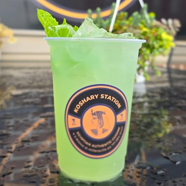 A Koshary Station branded cup of bright green iced mint lemonade with fresh mint leaves.
