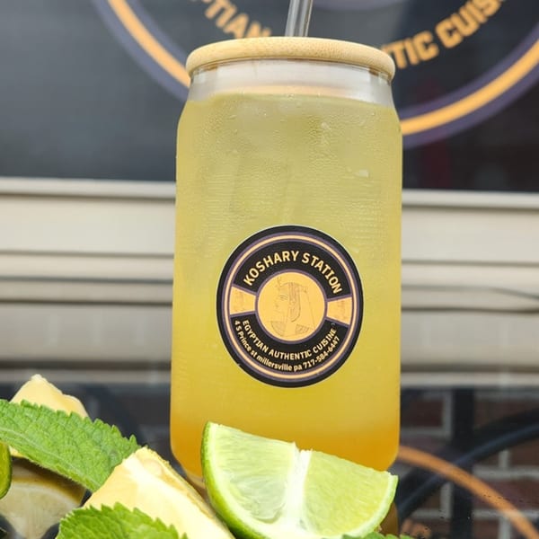 A cold Koshary Station drink with a logo, garnished with lime and mint.
